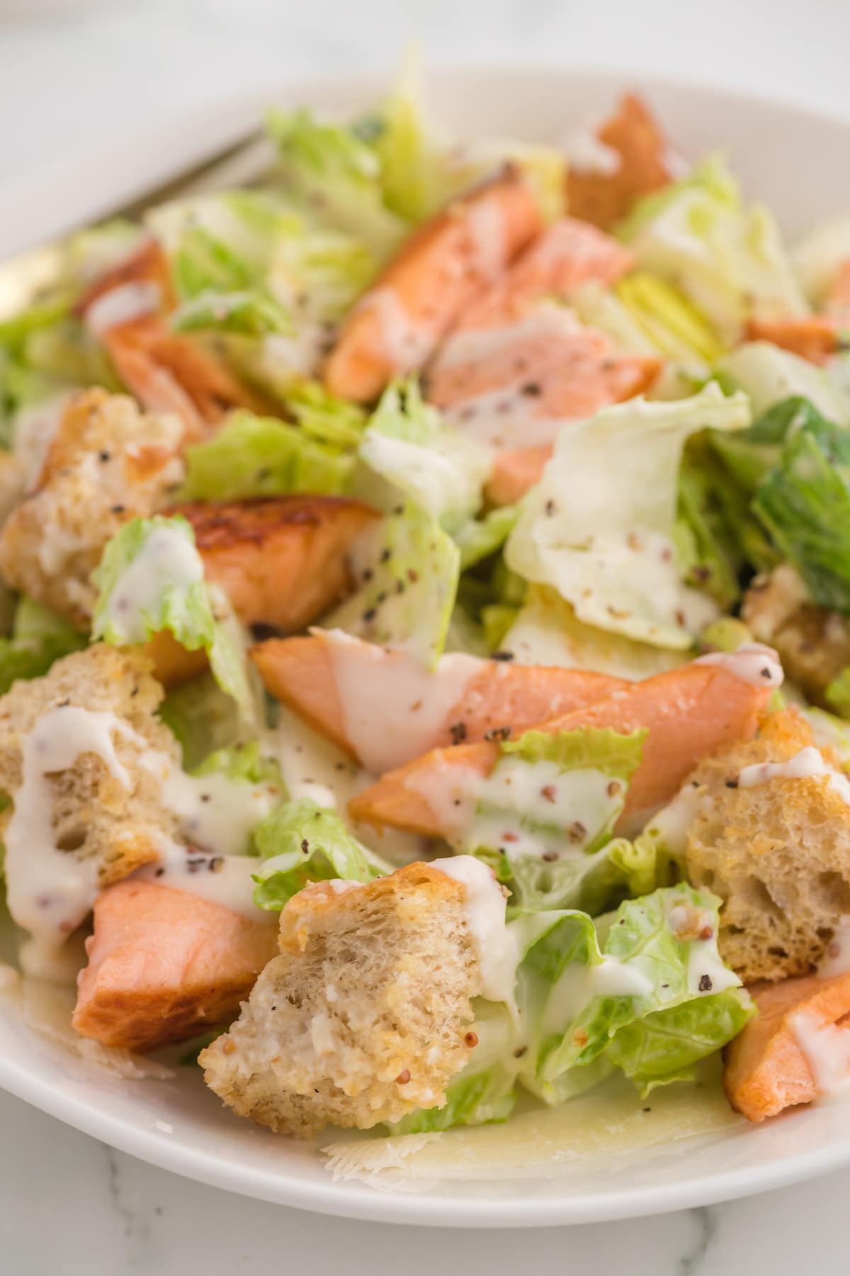 caesar salad with croutons in a white plate with pieces of salmon on top