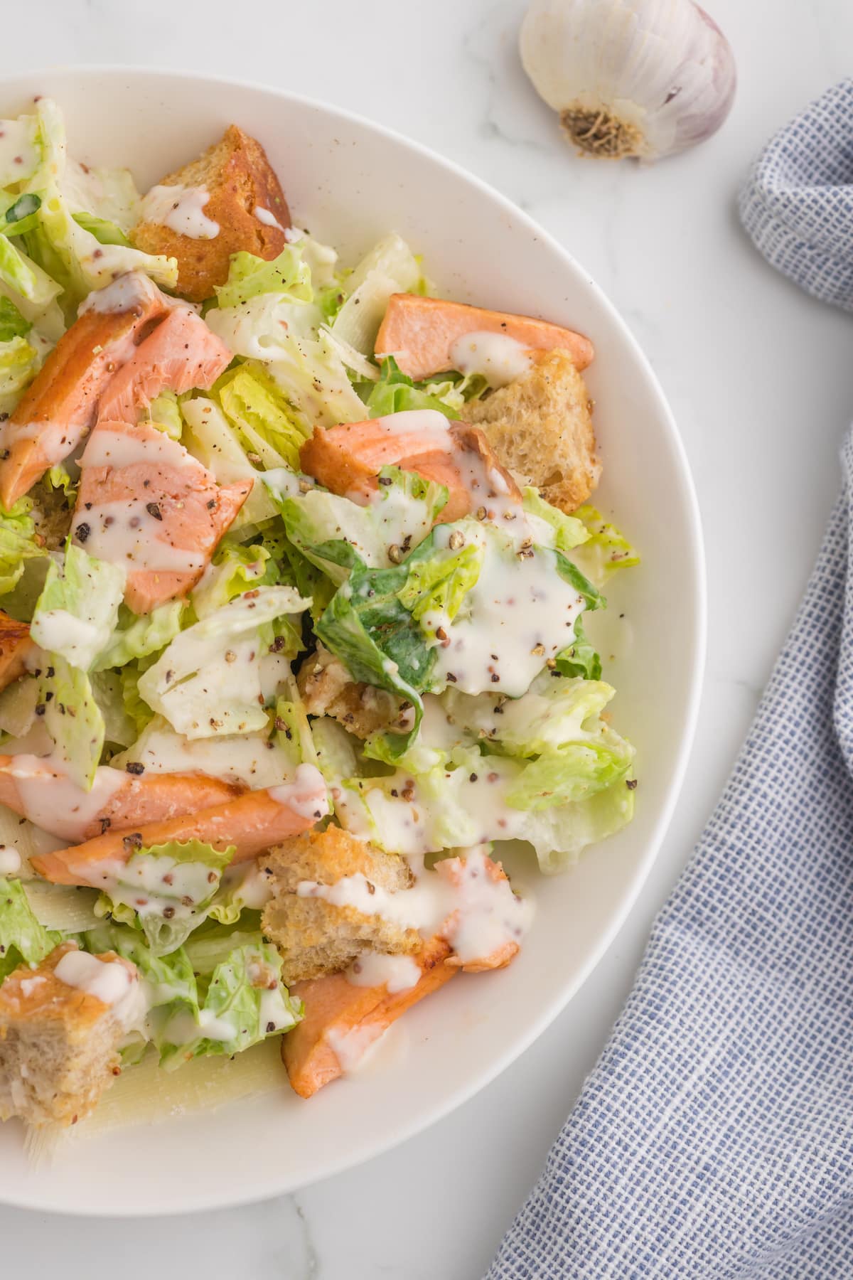 caesar salad with croutons in a white plate with pieces of a filet of salmon on top