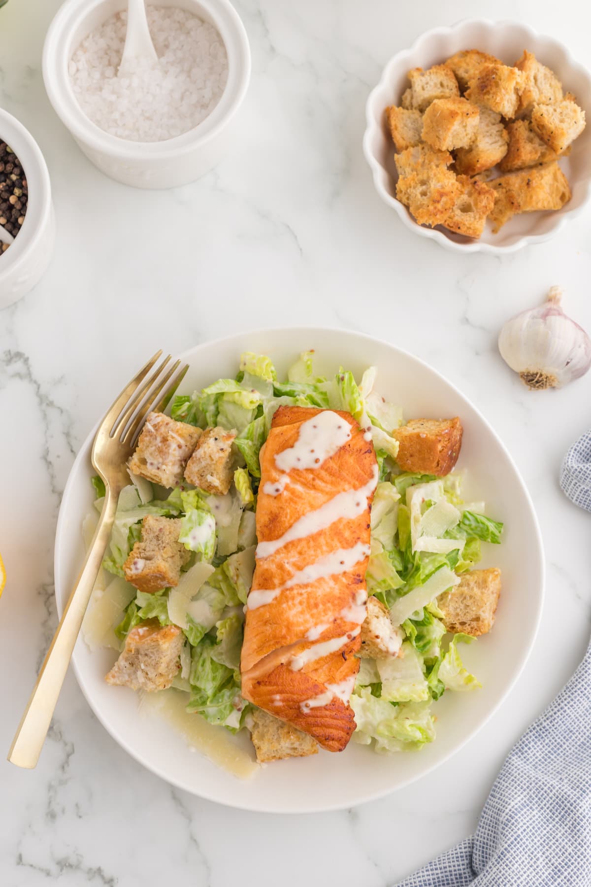 caesar salad with croutons in a white plate with a filet of salmon on top