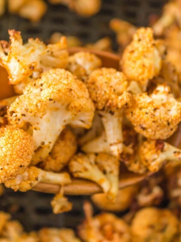 a wooden spoon lifting caramelized cauliflower from an air fryer