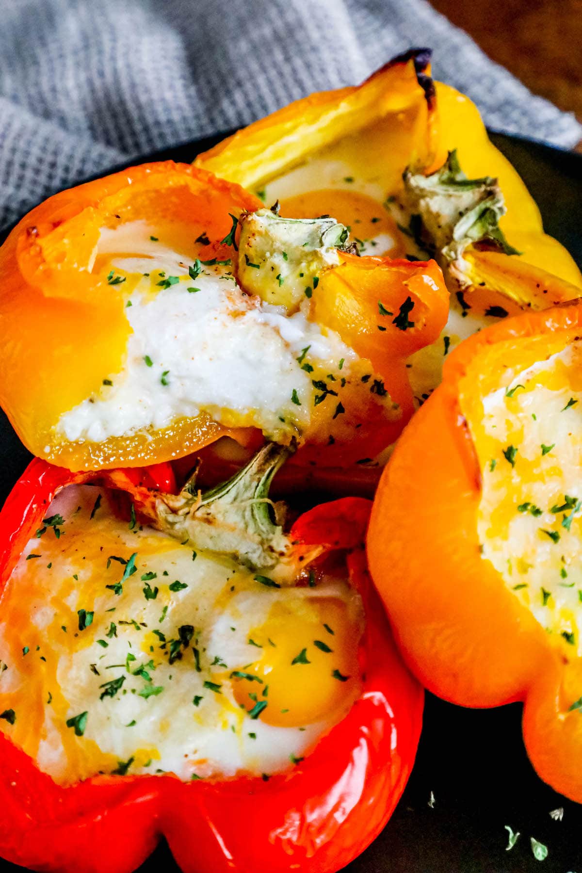baked eggs inside half of a yellow bell pepper with melted cheese and herbs on top on a black plate
