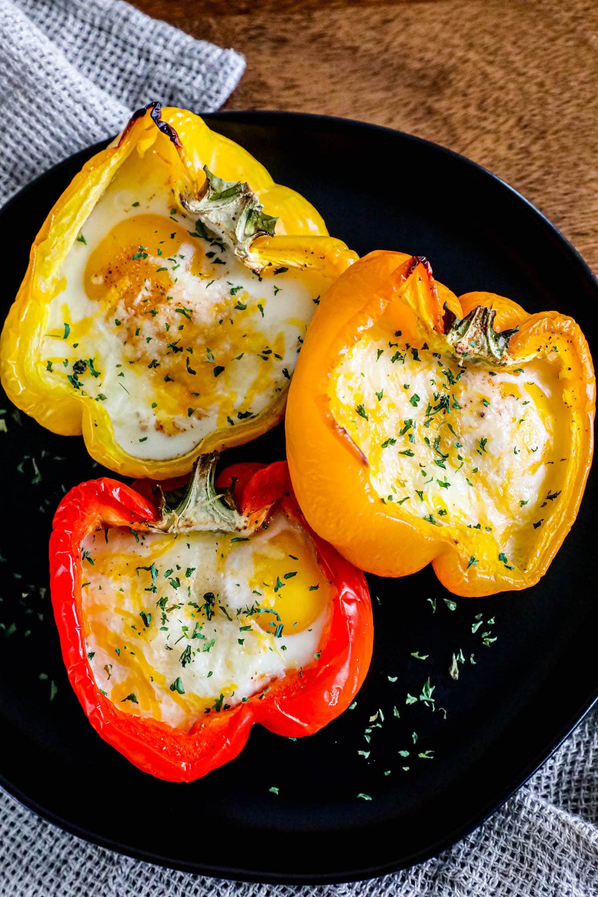 baked eggs inside half of a bell pepper with melted cheese and herbs on top on a black plate