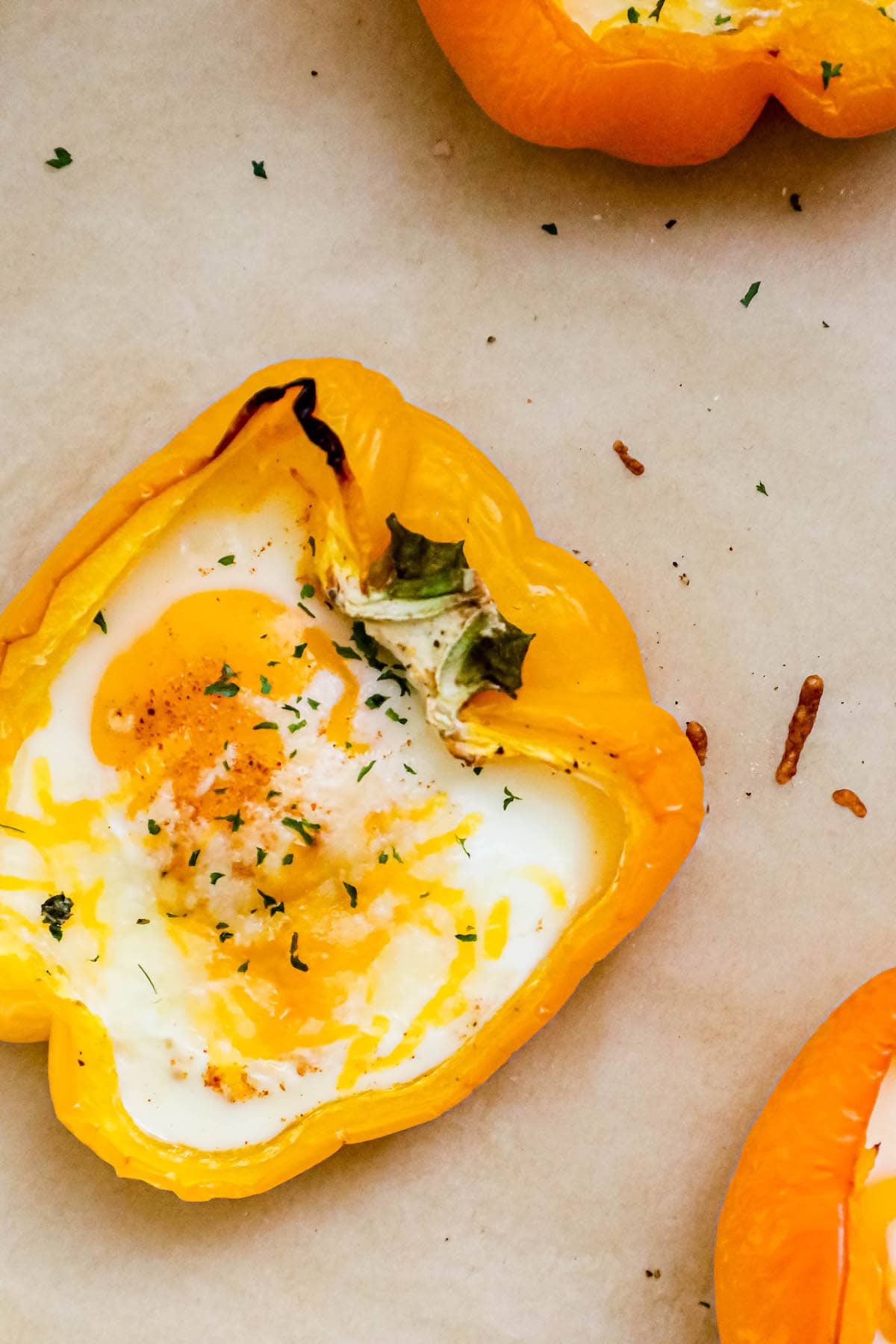 baked eggs inside half of a bell pepper with melted cheese and herbs on top on a baking sheet with parchment paper