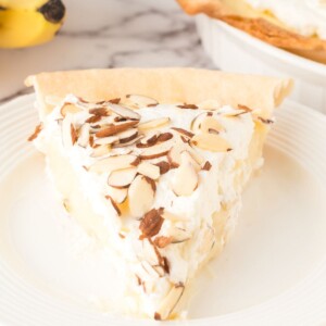 slice of banana cream pie with whipped topping and sliced almonds on top on a white plate