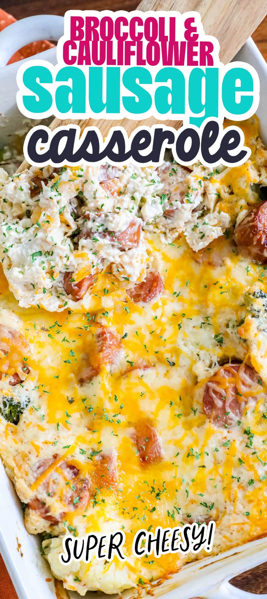 wooden spoon scooping baked cheesy casserole with sliced sausage, broccoli, cauliflower, and herb seasonings in a white casserole dish on a table