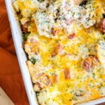 cheesy casserole with sliced sausage, broccoli, cauliflower, and herb seasonings in a white casserole dish on a table