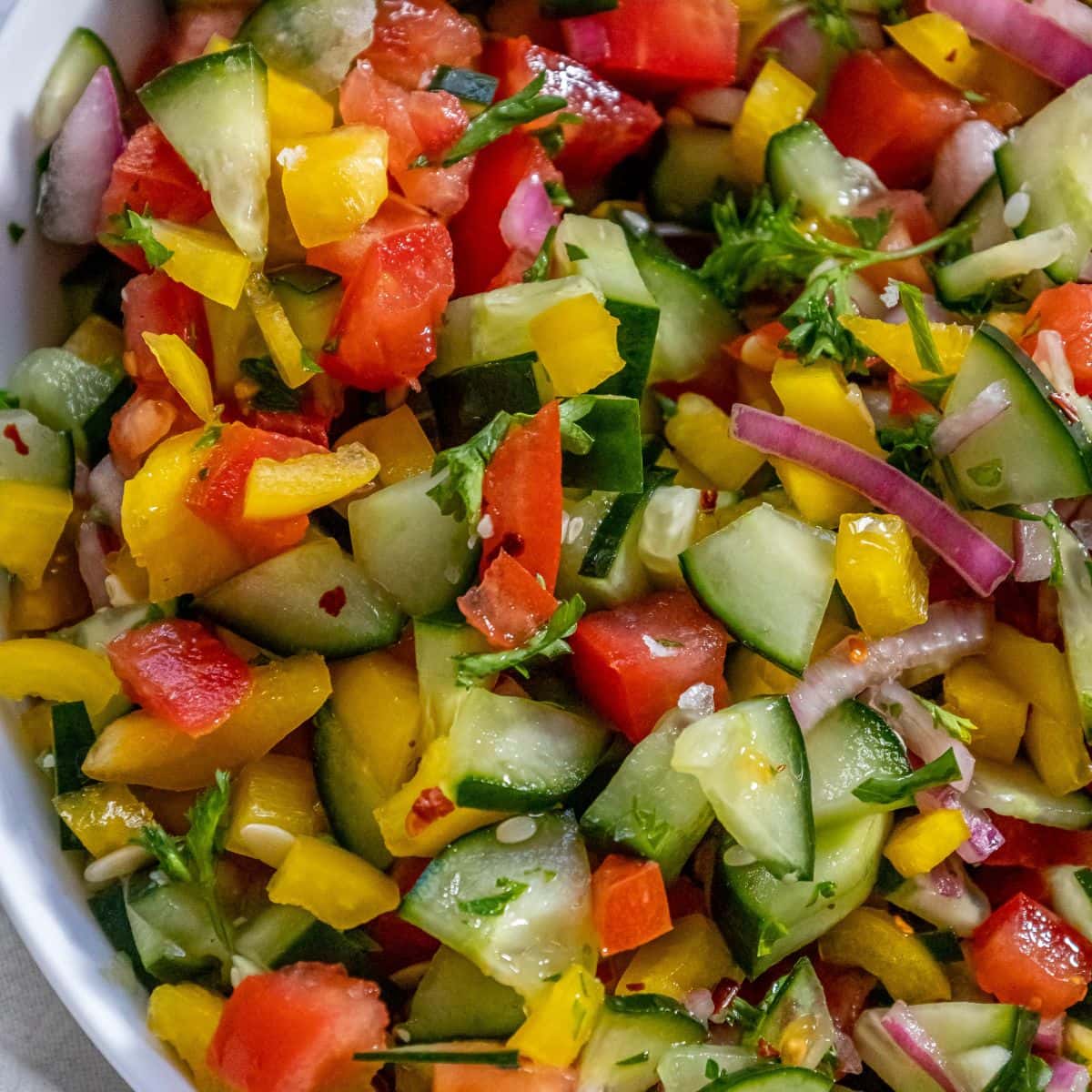 chopped bell pepper, cucumber, cherry tomatoes, red onion, and parsley in a white bowl