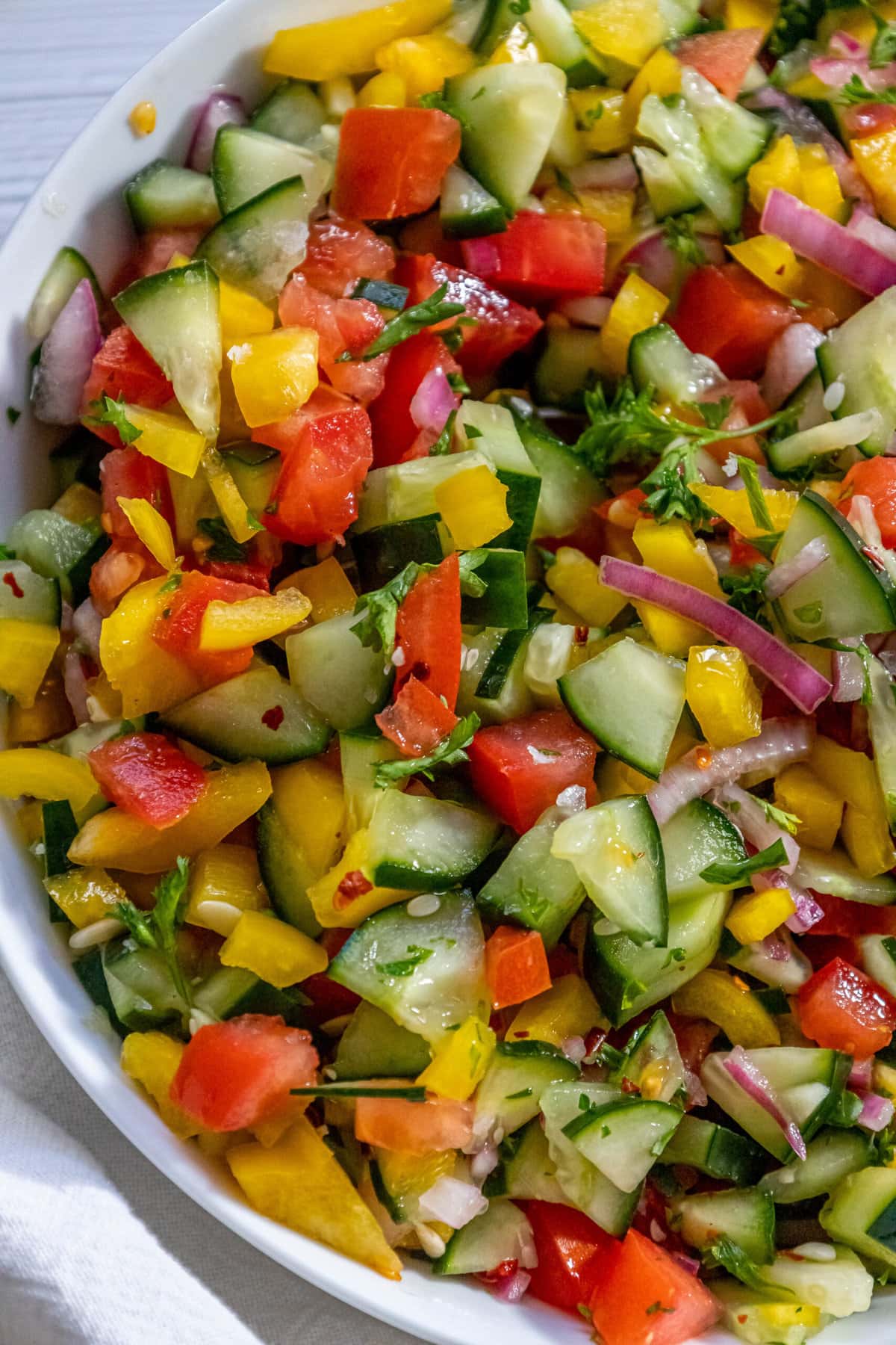 mixed salad of chopped bell pepper, cucumber, cherry tomatoes, red onion, and parsley in a white bowl