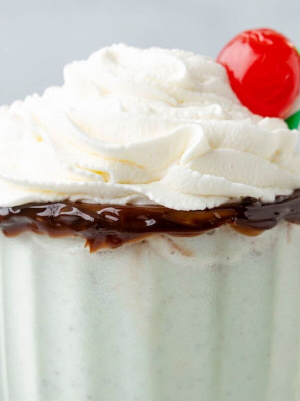 mint milkshake in a tall glass cup with whipped cream and a cherry on top, and a straw on the side