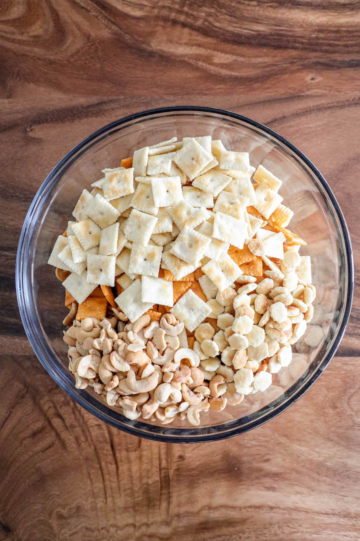 corn chips, corn cereal, pretzels, cheese crackers, nuts in a glass bowl