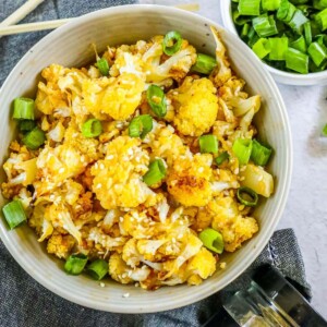 browned cauliflower with sesame seeds and chopped scallions in a white bowl on a table