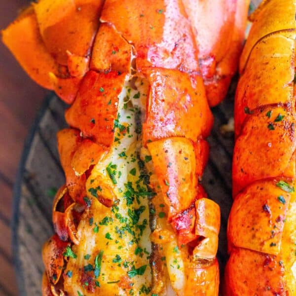 Two broiled lobster tails on a wooden board.