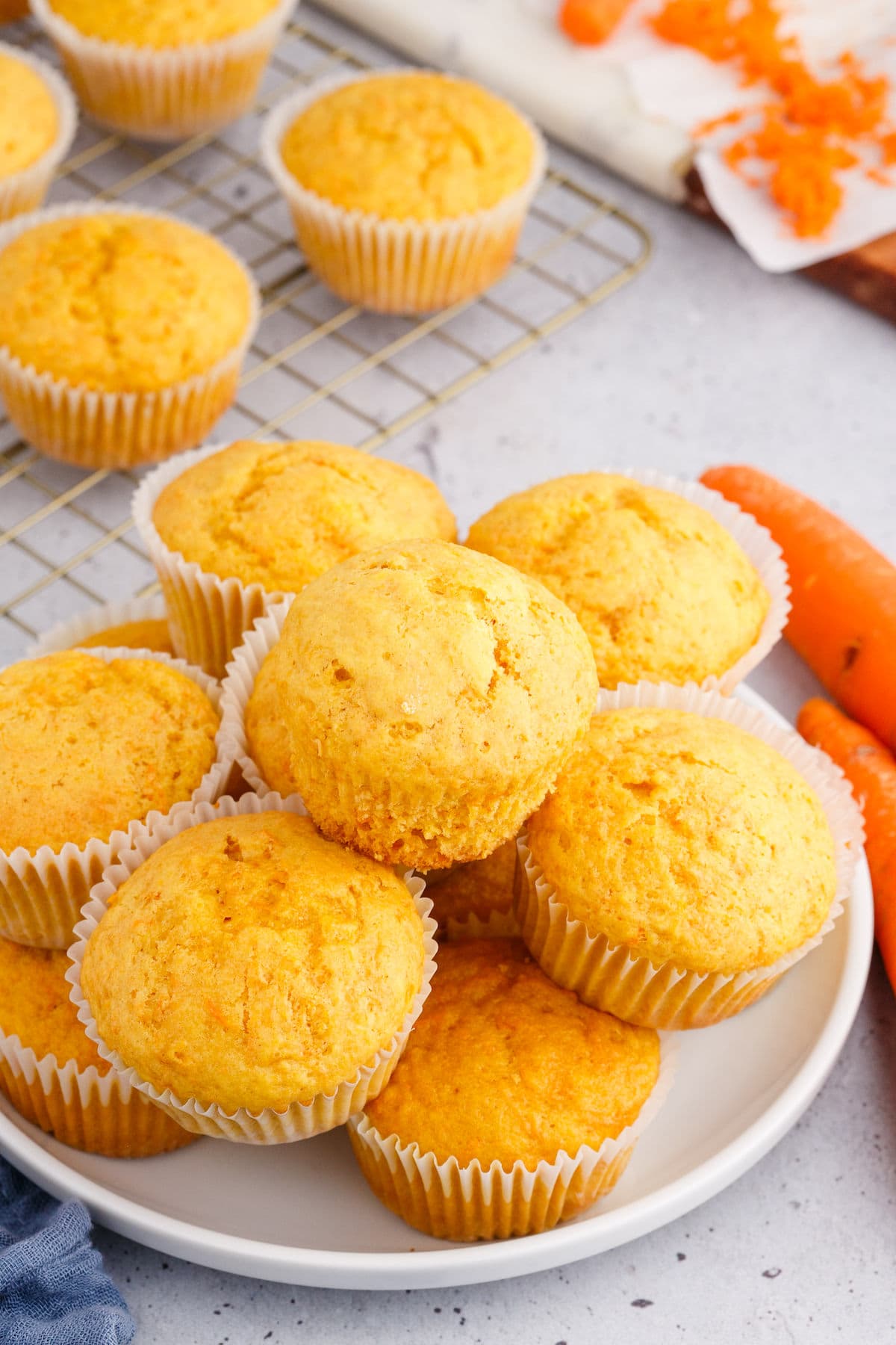 carrot muffins with white cupcake liners stacked on a plate on a table