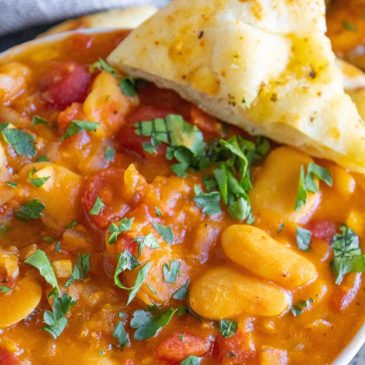 baked greek beans in a tomato sauce with chopped herbs and giant white beans