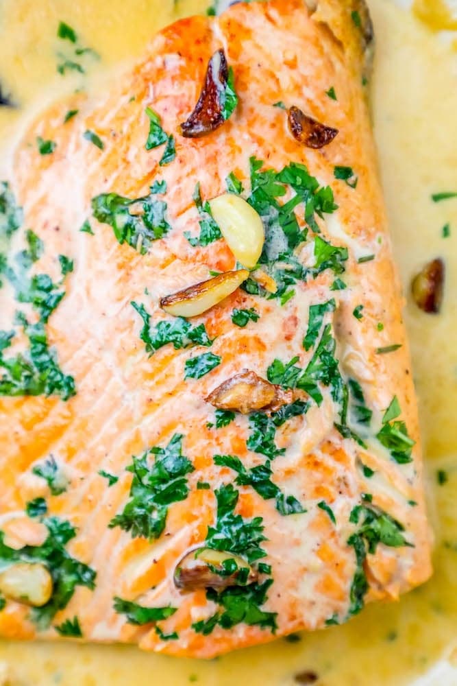 whiskey cream sauce salmon topped with chopped parsley and garlic cloves on top 