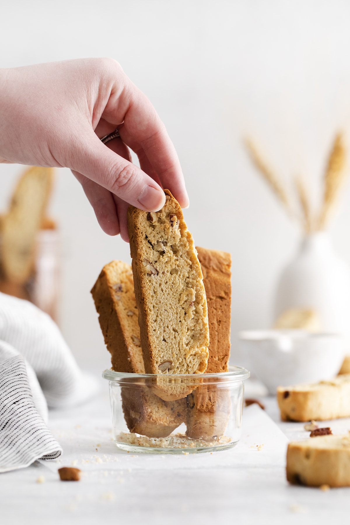 a hand grabbing a baked biscotti with pecan in a jar on a table