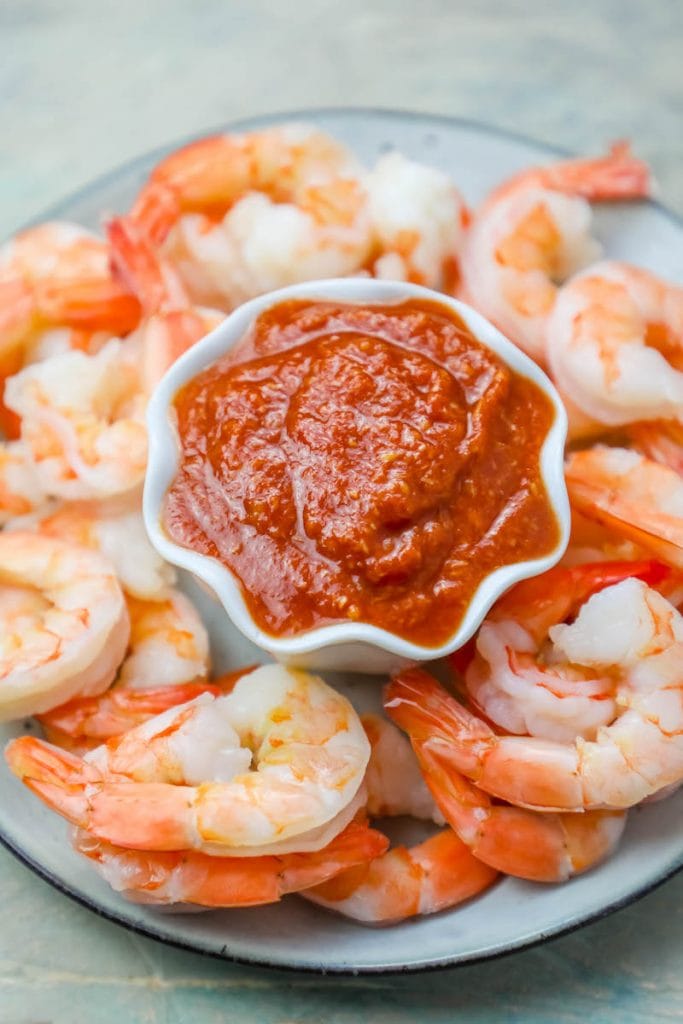 cooked shrimp cocktail on a plate around a cup of bright red cocktail sauce