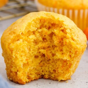 a baked carrot muffin with a big bite taken out of it, showing the light airy texture of the muffin inside