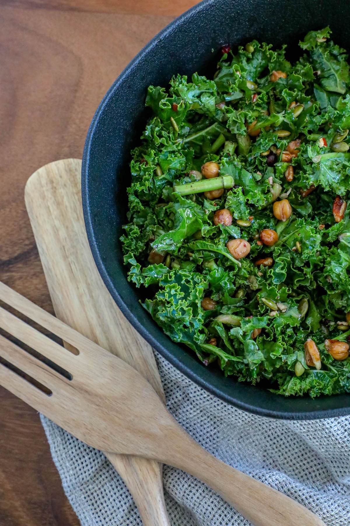 kale salad in a bowl with chickpeas, dried cranberries, pomegranate arils, pepitas, and dressing