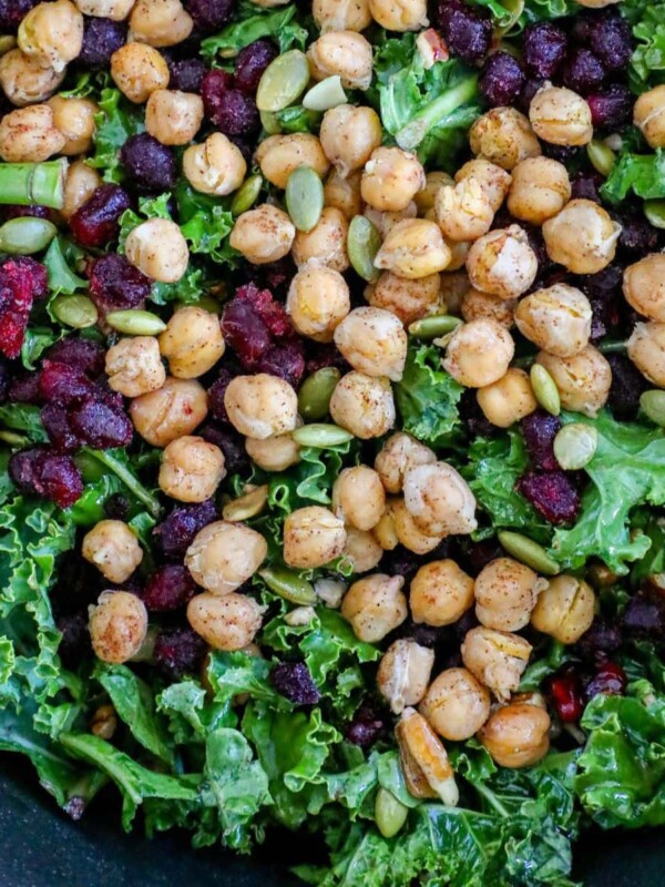 chickpeas, kale, dried cranberries, pomegranate arils, pepitas, dressing, sunflower seeds in a bowl