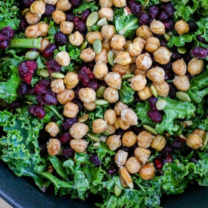 chickpeas, kale, dried cranberries, pomegranate arils, pepitas, dressing, sunflower seeds in a bowl