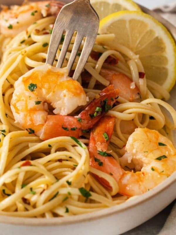 shrimp and pasta in a bowl with slices of lemon, herbs, and red pepper flakes