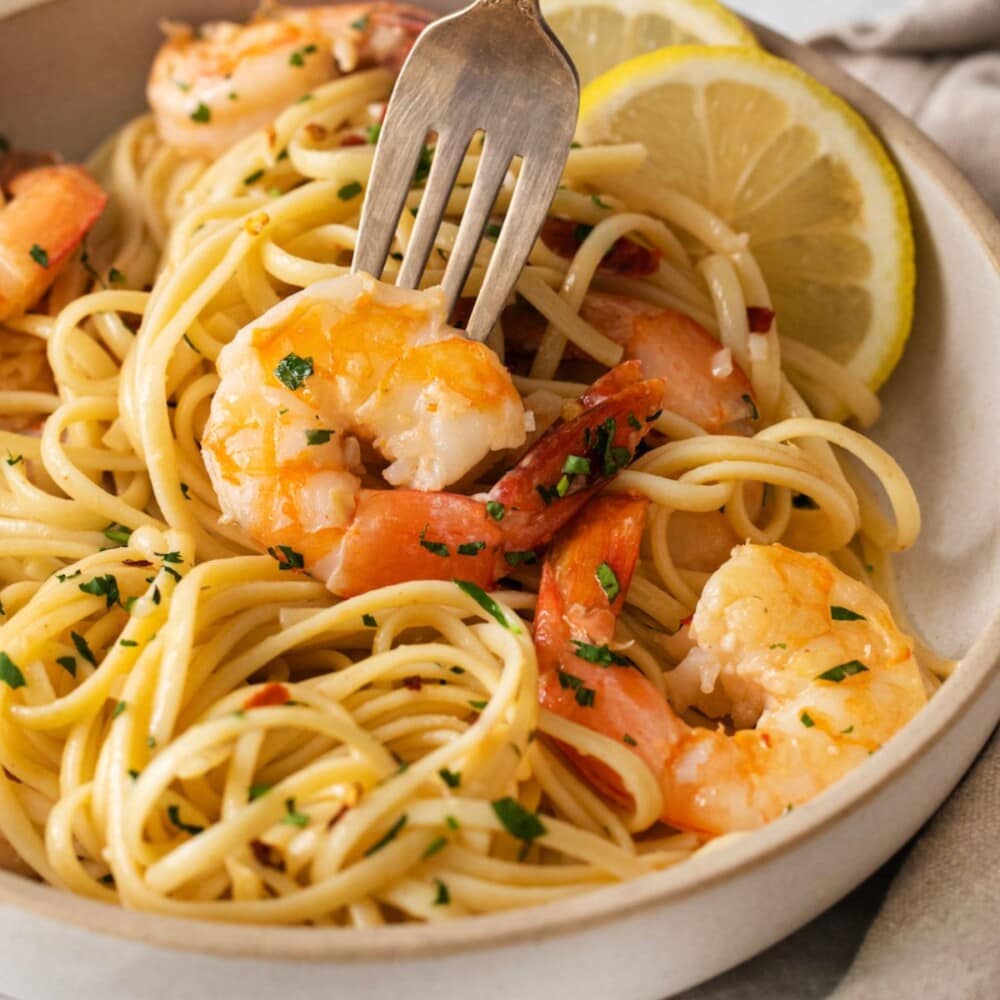 shrimp and pasta in a bowl with slices of lemon, herbs, and red pepper flakes