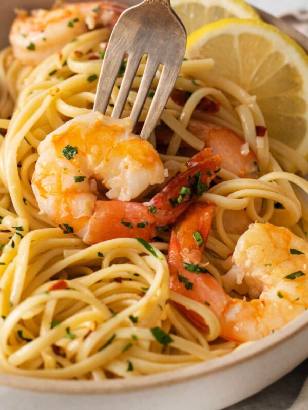 shrimp and pasta in a bowl with slices of lemon, herbs, and red pepper flakes