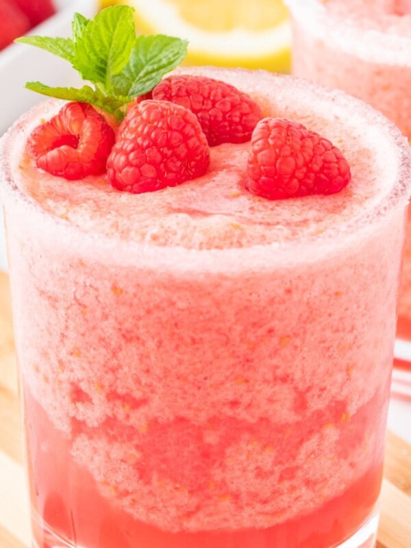 frozen pink lemonade in a sugar rimmed glass with raspberries and a sprig of mint on top