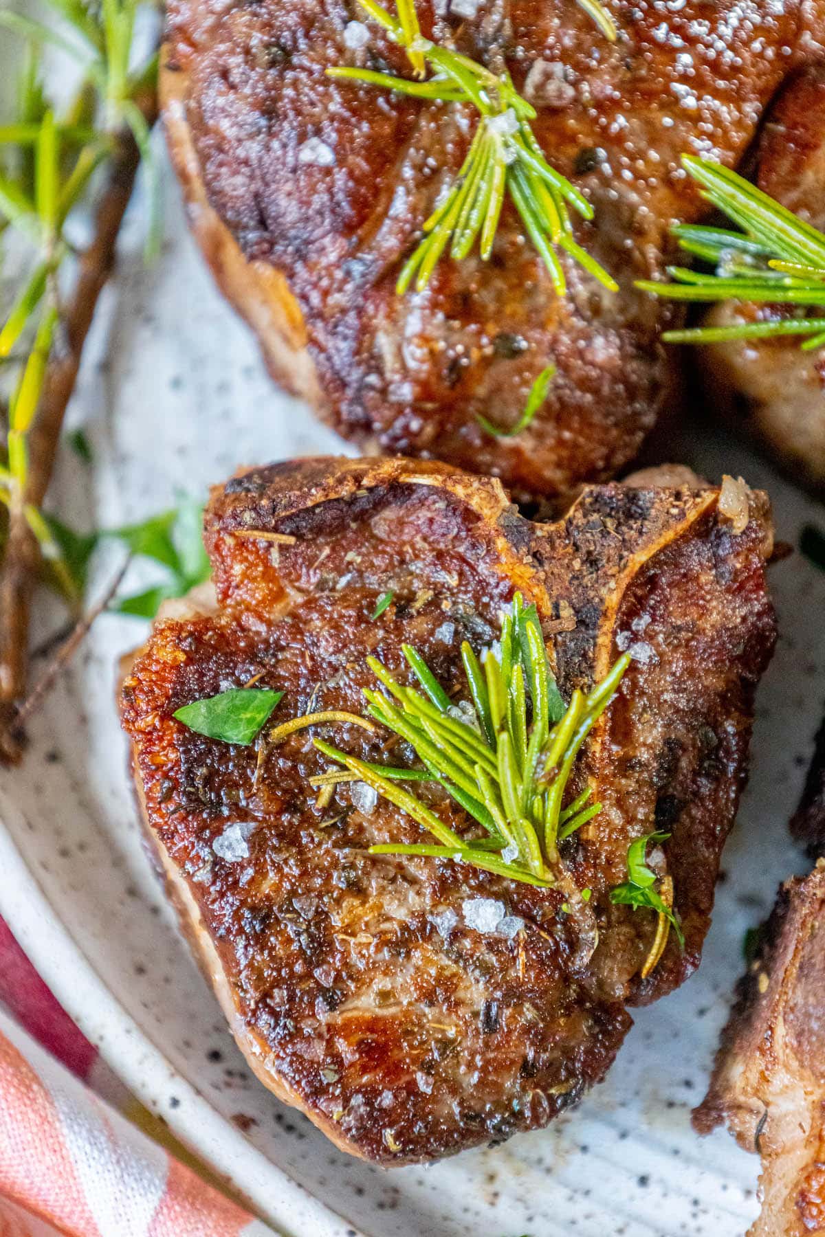 seared lamb chop on a white plate with a sprig of rosemary and sea salt flakes on top 