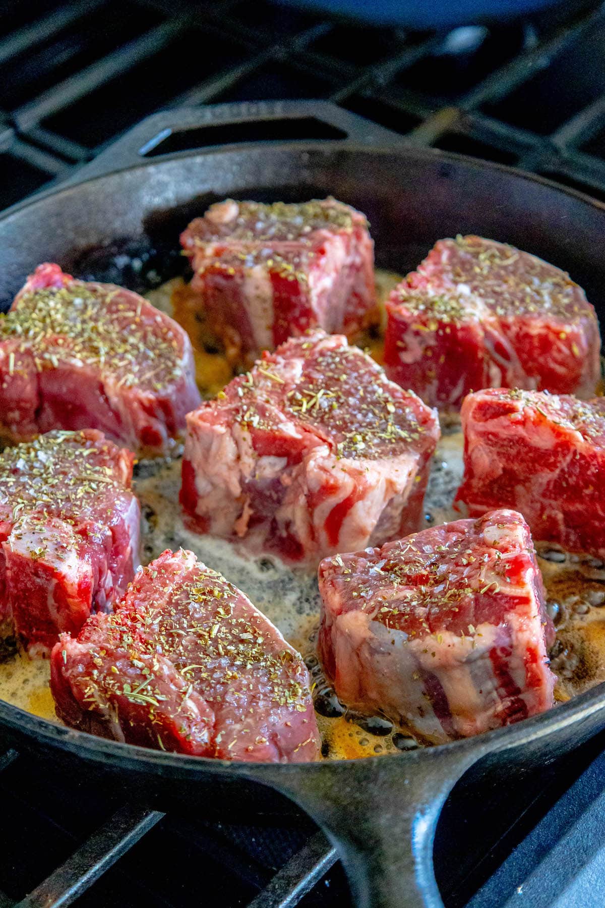 seasoned raw lamb chops in a cast iron pan with melted butter