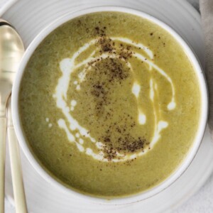 asparagus soup in a white bowl with a swirl of cream on top and a crack of pepper