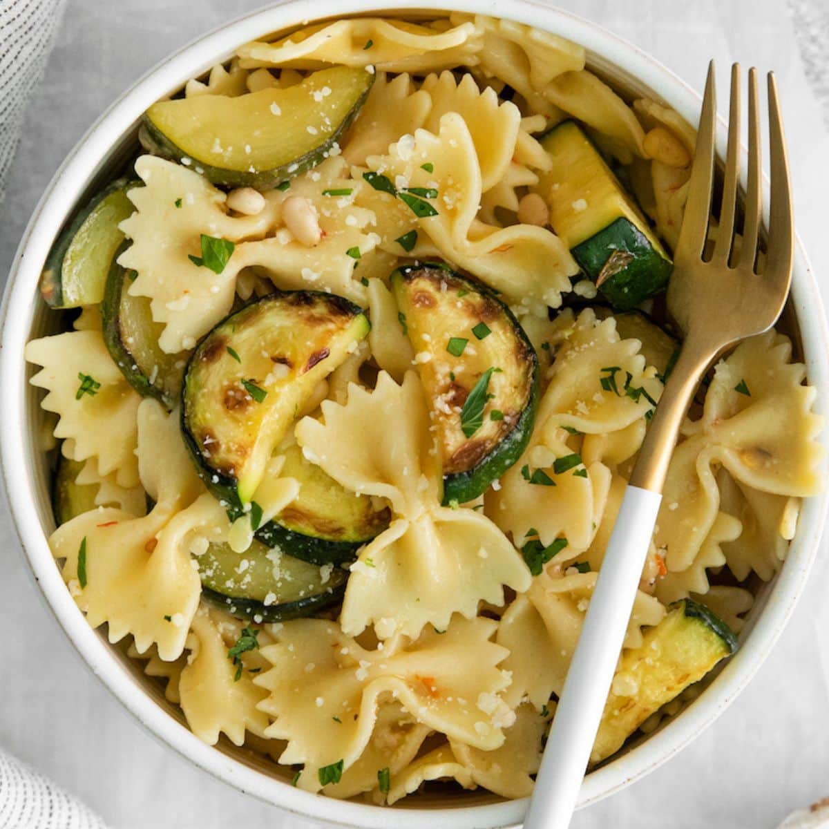 bowtie pasta in a white bowl with zucchini slices, pine nuts, herbs