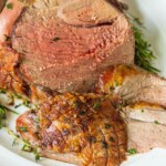 a roasted leg of lamb sliced open on a cutting board and topped with chopped herbs