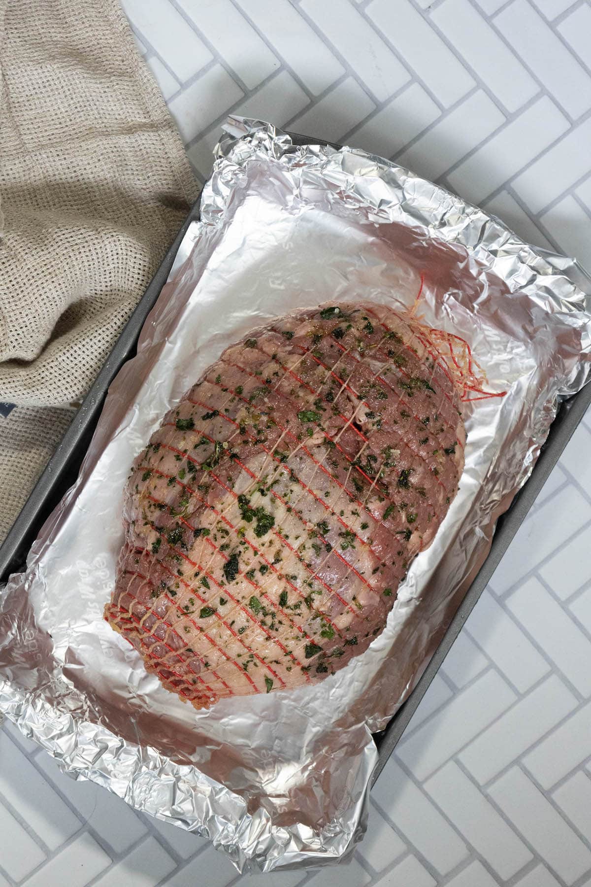 raw leg of lamb covered in olive oil, herbs, and salt