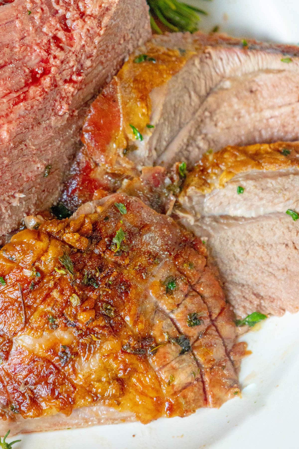 a roasted leg of lamb sliced open on a white platter and topped with chopped herbs