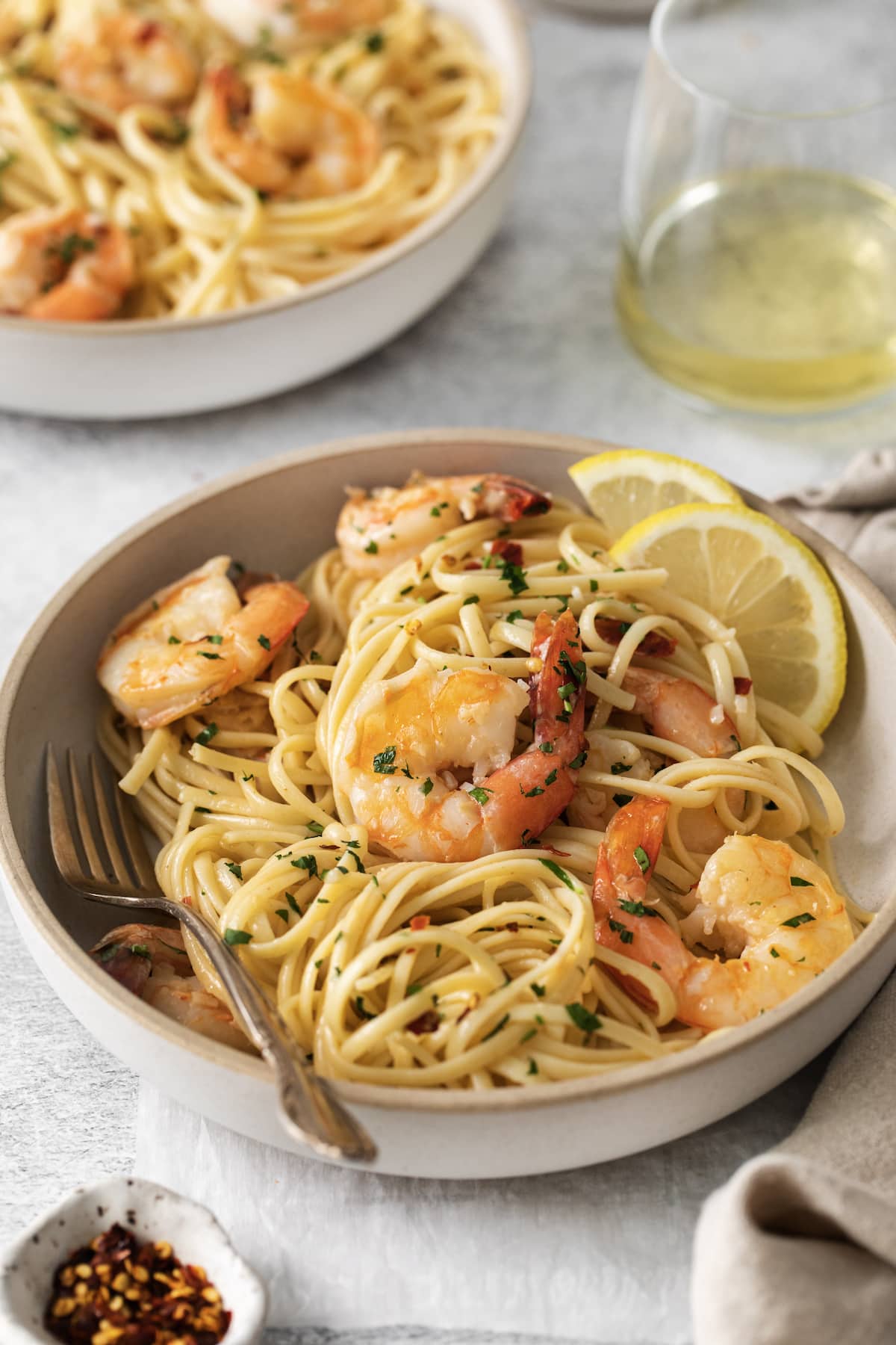 shrimp pasta with linguine, red pepper flakes, herbs, and lemon slices in a bowl