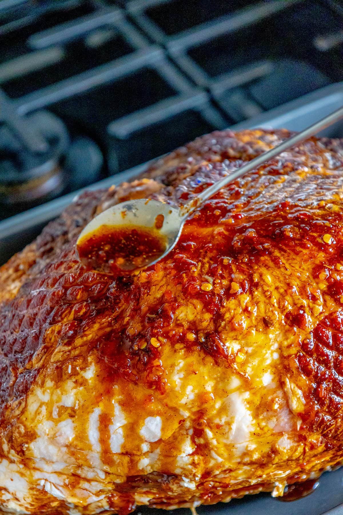 A honey soy spiral ham roasted in a pan with a spoon.