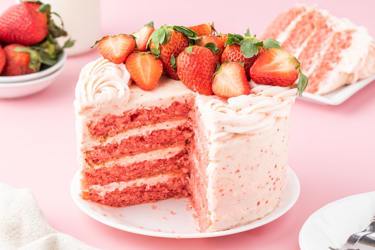 fresh sliced strawberries on a pink frosted cake with layers of whipped pink icing that has strawberry bits in it 