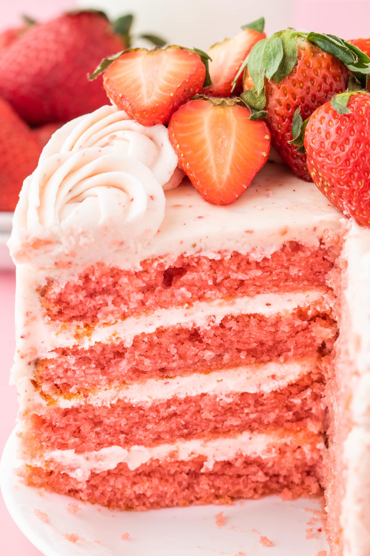 fresh sliced strawberries on a pink frosted cake with layers of whipped pink icing that has strawberry bits in it 