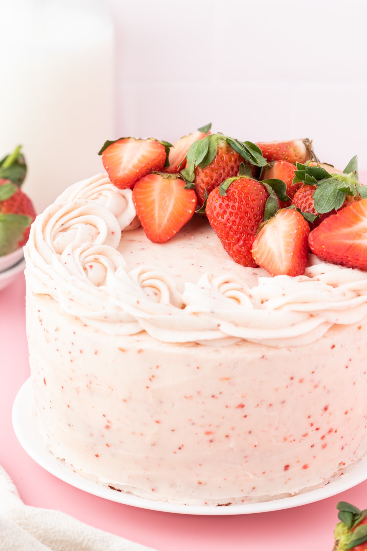 fresh sliced strawberries on a pink frosted cake with bits of strawberry in the whipped icing