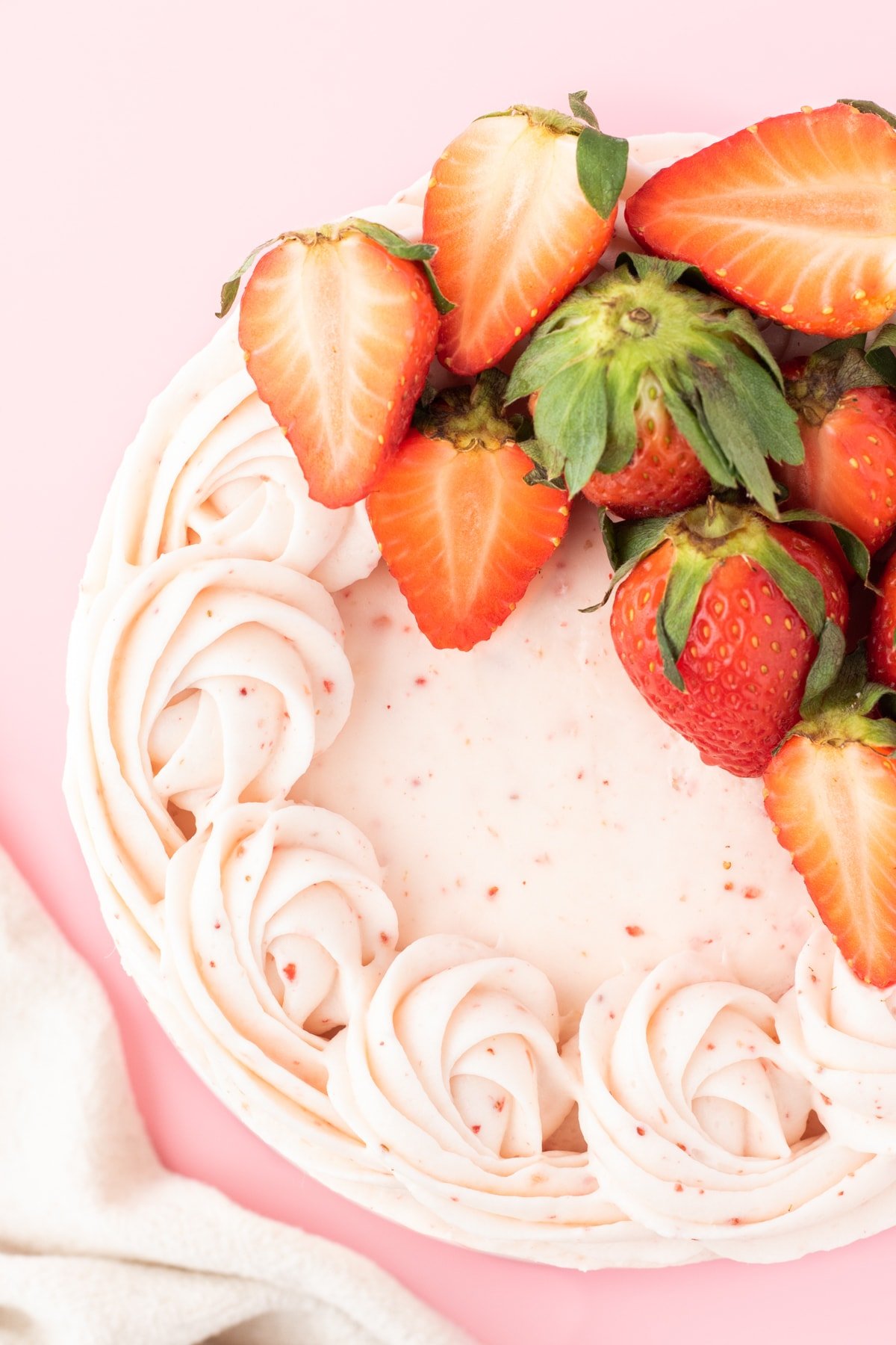 fresh sliced strawberries on top of a pink frosted cake with swirls of pink whipped icing on top 