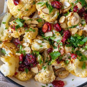 roasted cauliflower in creamy tahini sauce in a bowl with craisins, sliced almonds, and chopped parsley