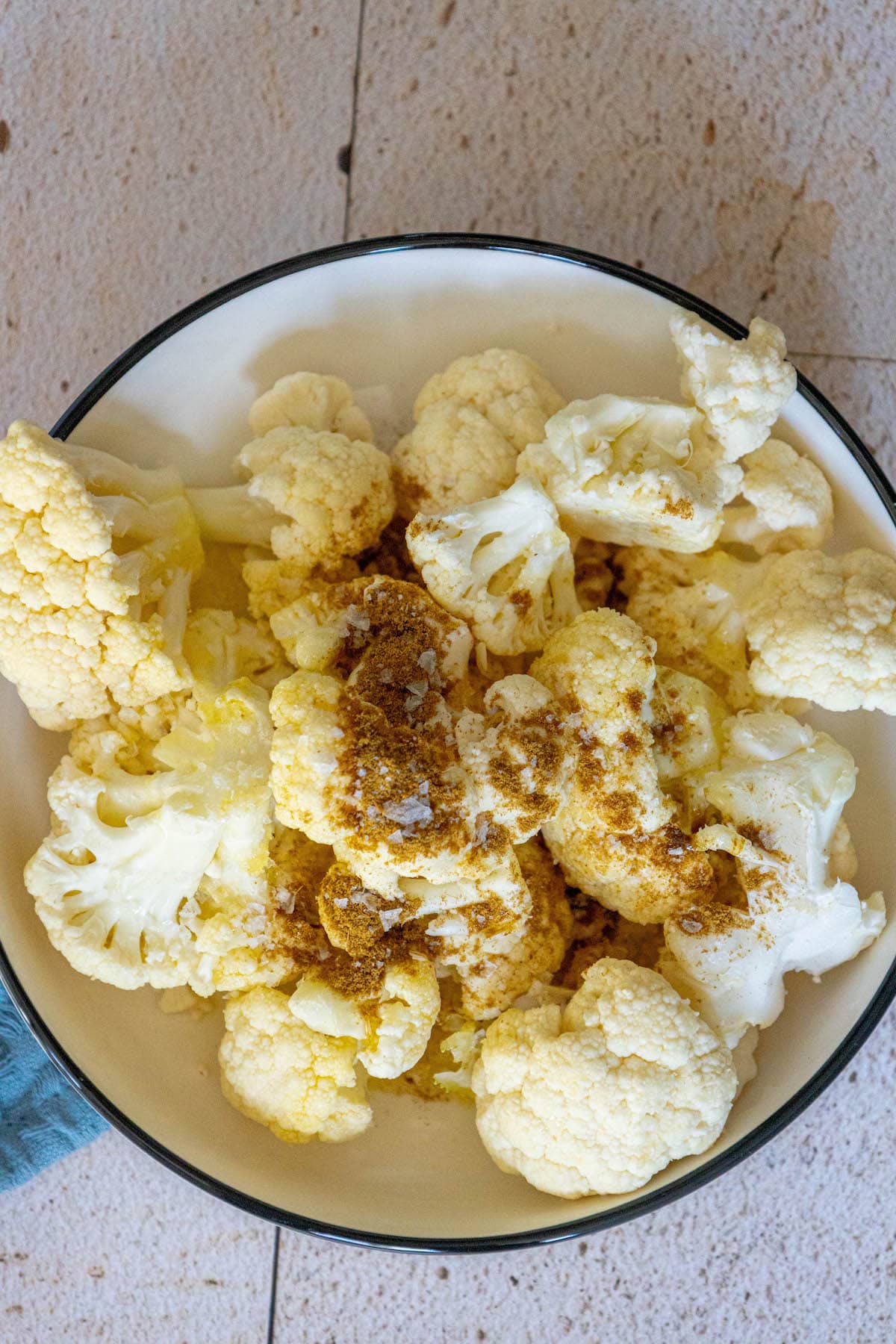 cauliflower in a bowl with olive oil, herbs, and salt
