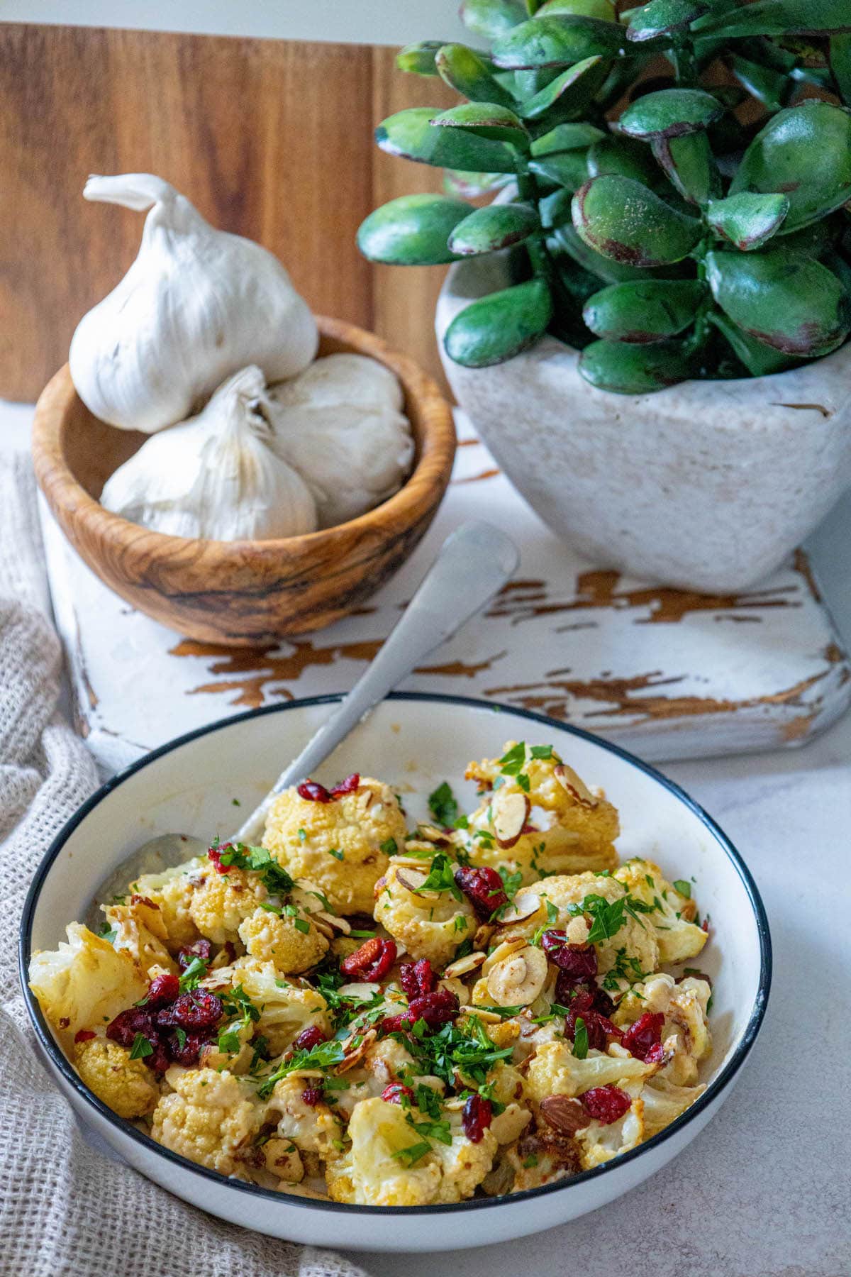 roasted cauliflower tossed in tahini sauce with cranberries, almonds, and chopped parsley in a white dish 