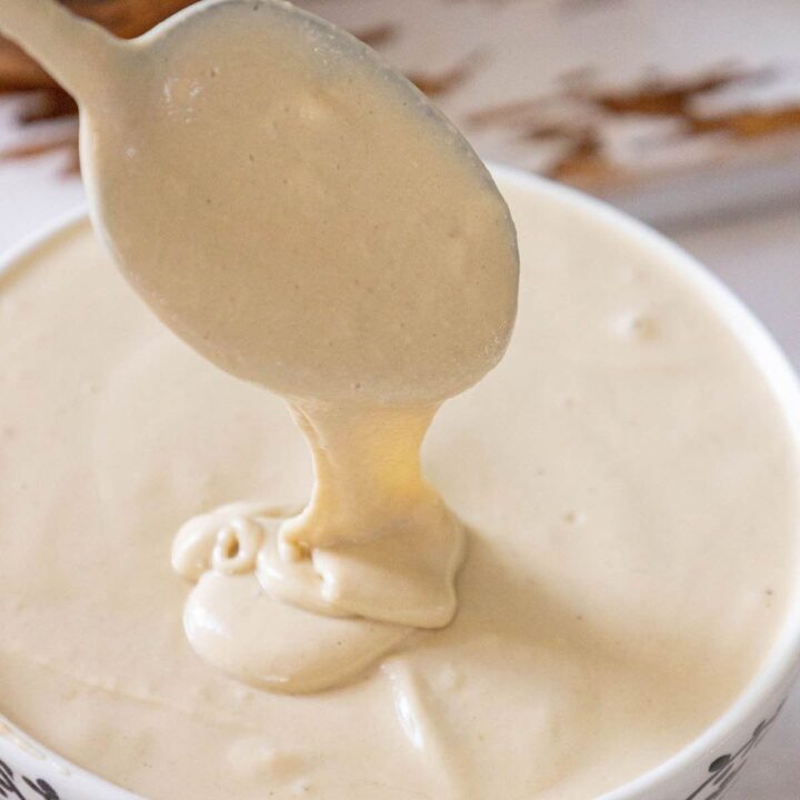 a spoon lifting tahini sauce over a bowl on a table