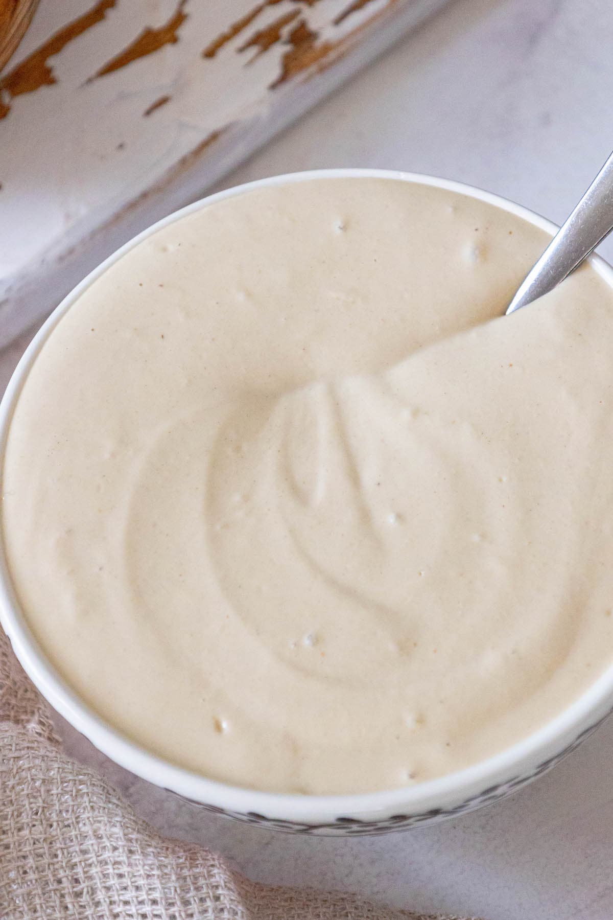 a spoon in a bowl of tahini sauce on a table