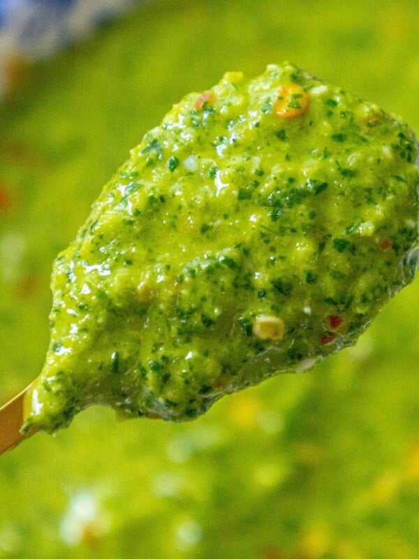 bright green sauce with flecks of cilantro and red pepper flakes on a spoon over a bowl of zhoug sauce