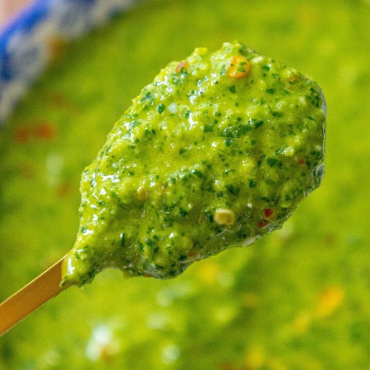bright green sauce with flecks of cilantro and red pepper flakes on a spoon over a bowl of zhoug sauce