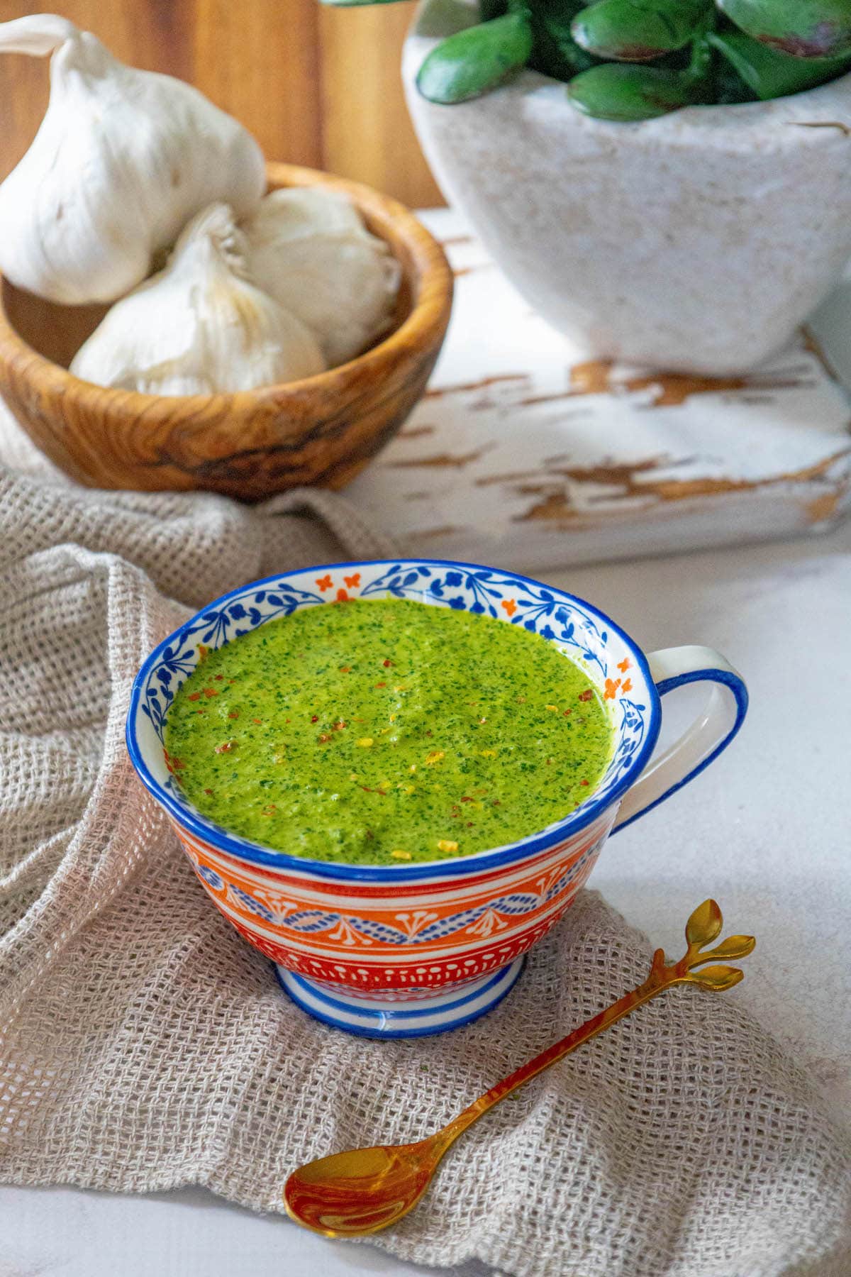 bright green zhoug sauce with flecks of cilantro and red pepper flakes in a mug on a table